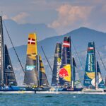 A group of sailboats in the water with mountains behind them.