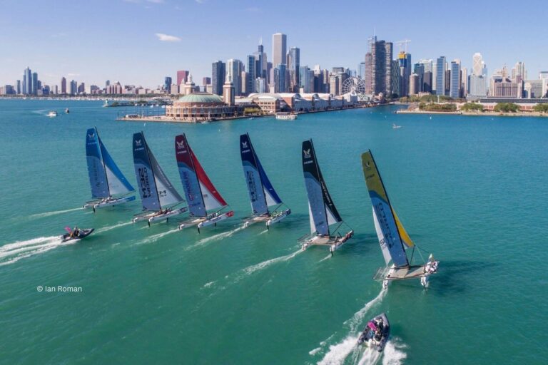 A group of sailboats in the water with city skyline in background.