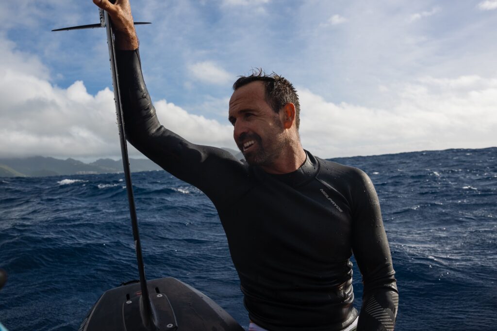 A man in black wetsuit holding onto a pole